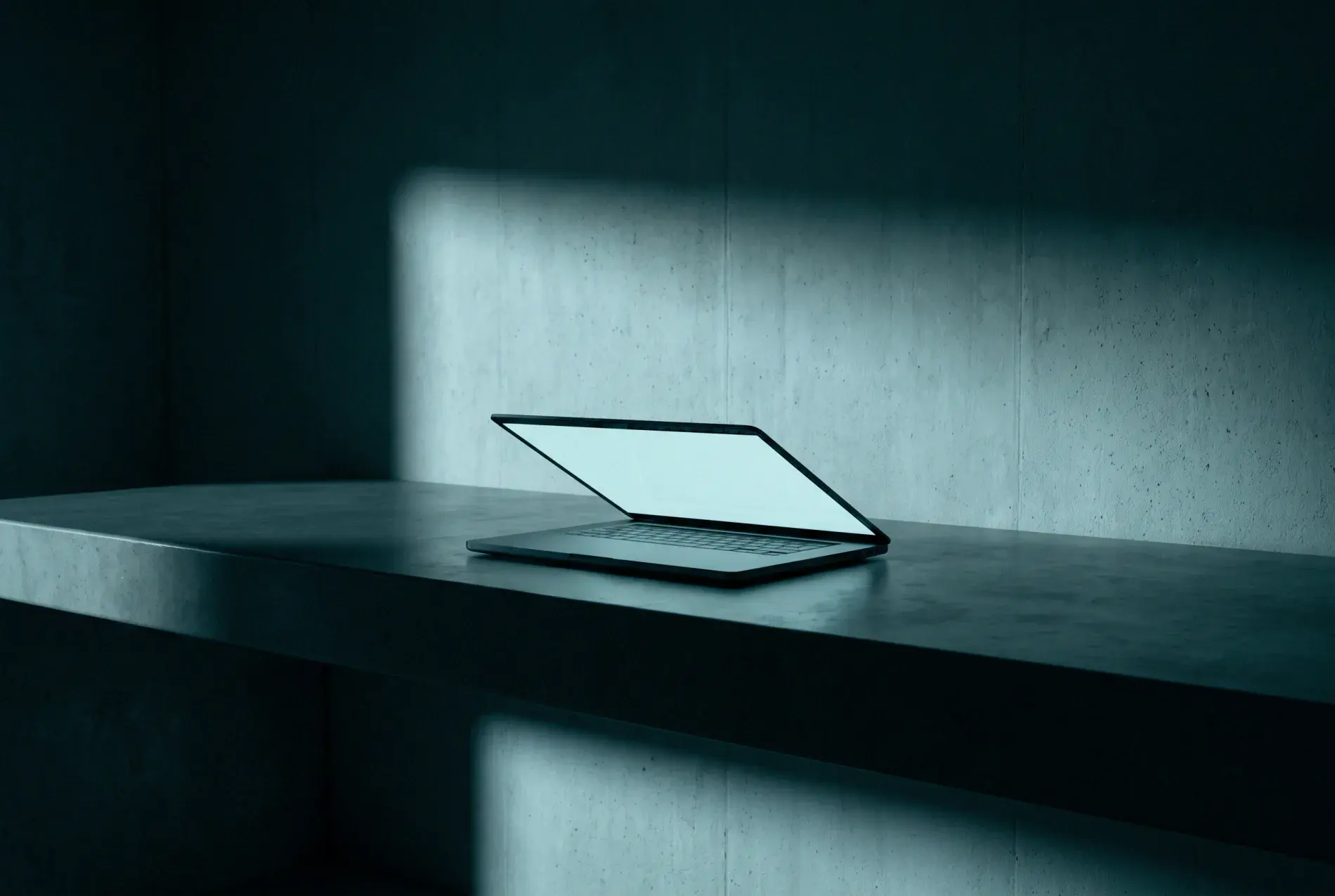 An open laptop lit on a concrete ledge in a dark room